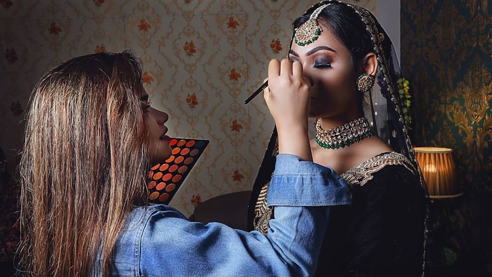 A makeup artist applying party makeup to a woman in festive jewellery