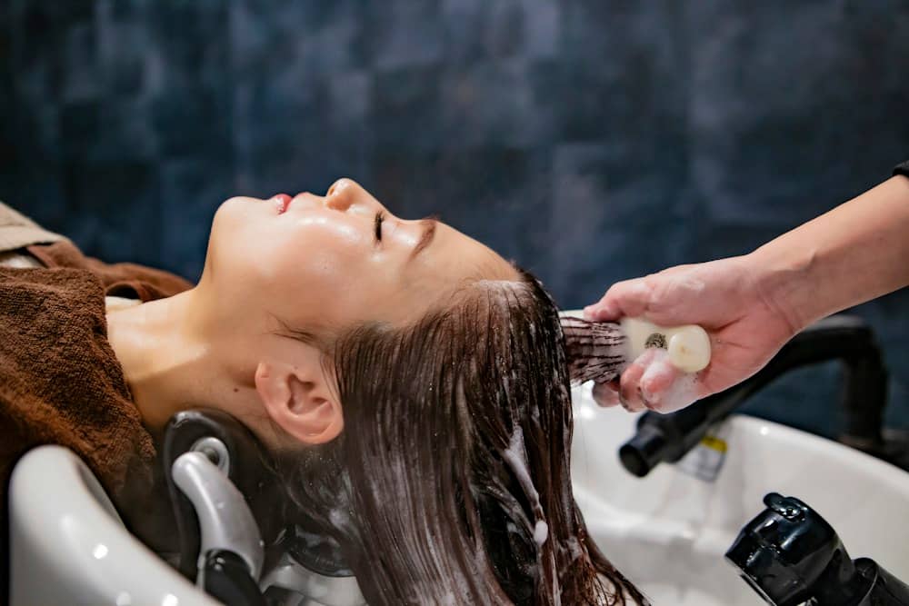 A hair specialist rinsing a client’s hair at the basin